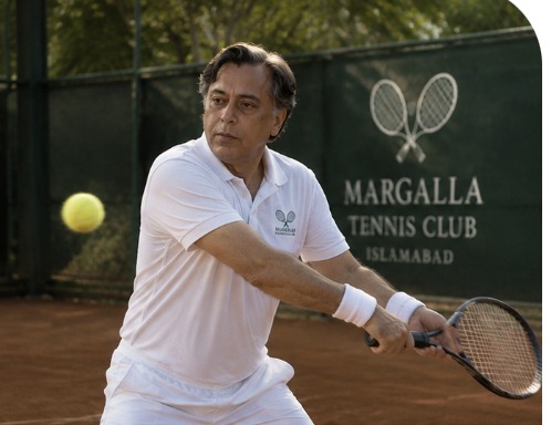 Etzaz “ET” Azim striking a backhand on the clay court beside the Margalla Tennis Club board