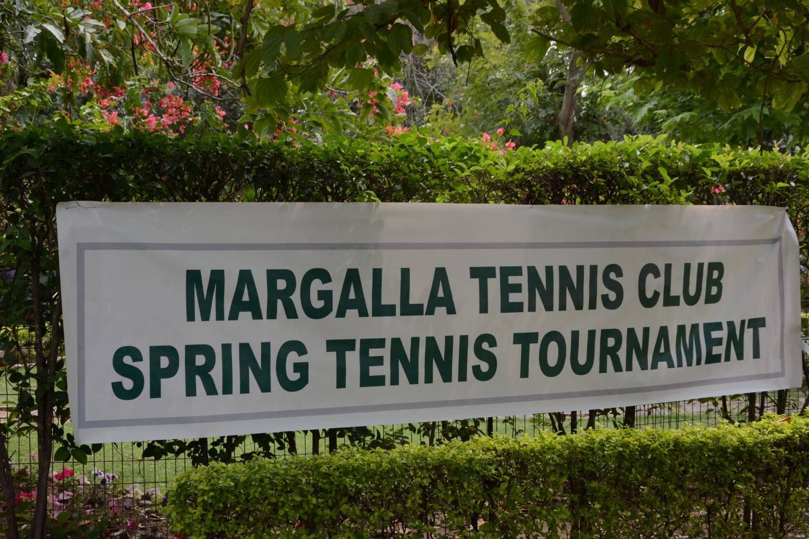 Margalla Tennis Club Spring Tennis Tournament banner hung on the hedge at the club entrance