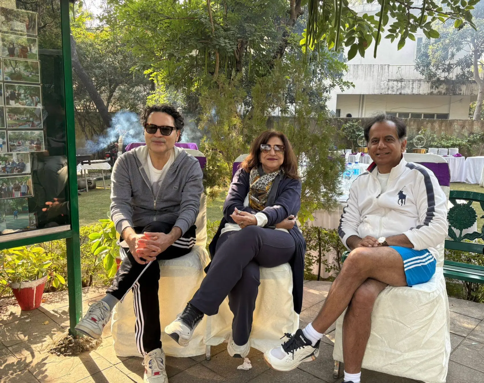Three members seated beside the club noticeboard in the garden